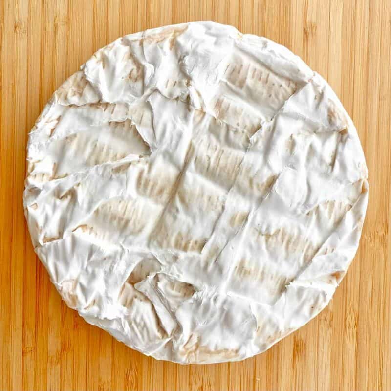 A 1 pound wheel of Brie Cheese on a wooden cutting board.