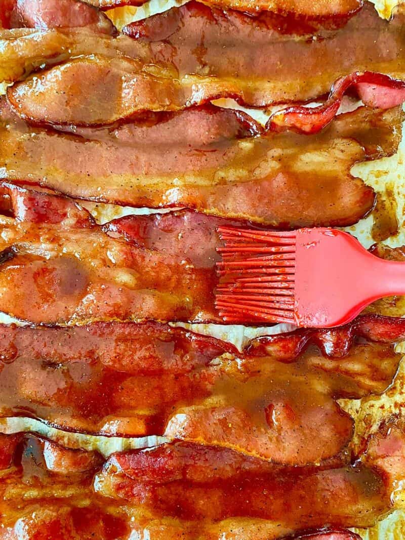 Brushing glaze on partially cooked bacon using a red silicone pastry brush.