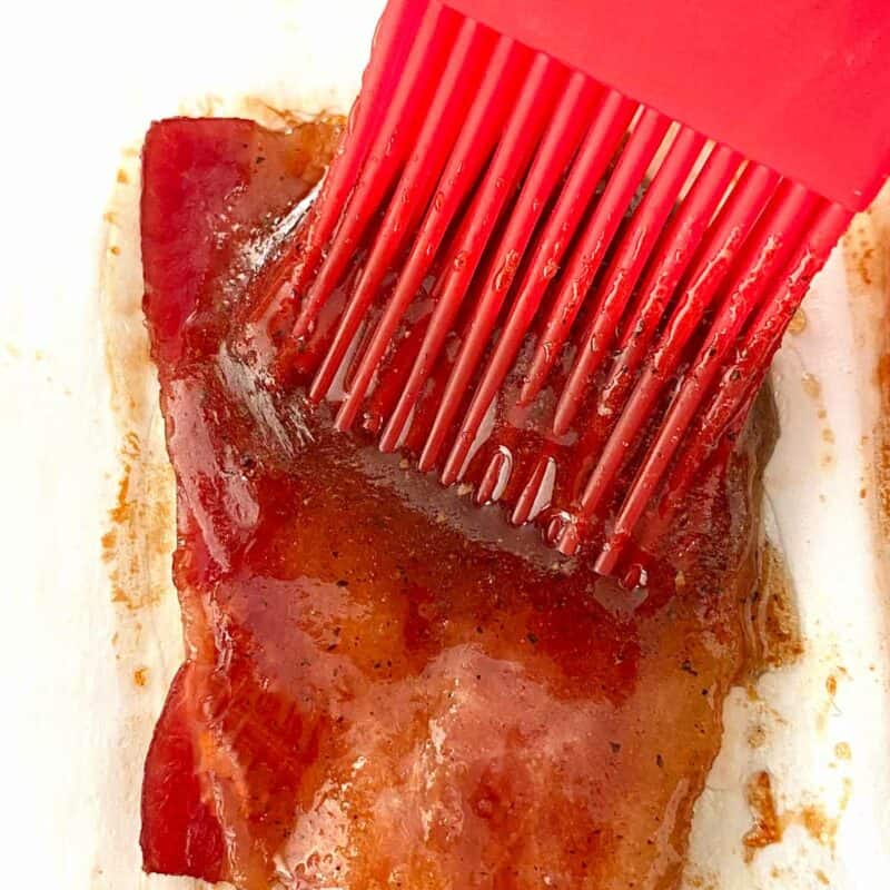 Brushing brown sugar glaze on bacon with a red pastry brush.
