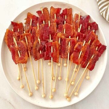 Two dozen brown sugar candied bacon lollipops on a white serving tray.