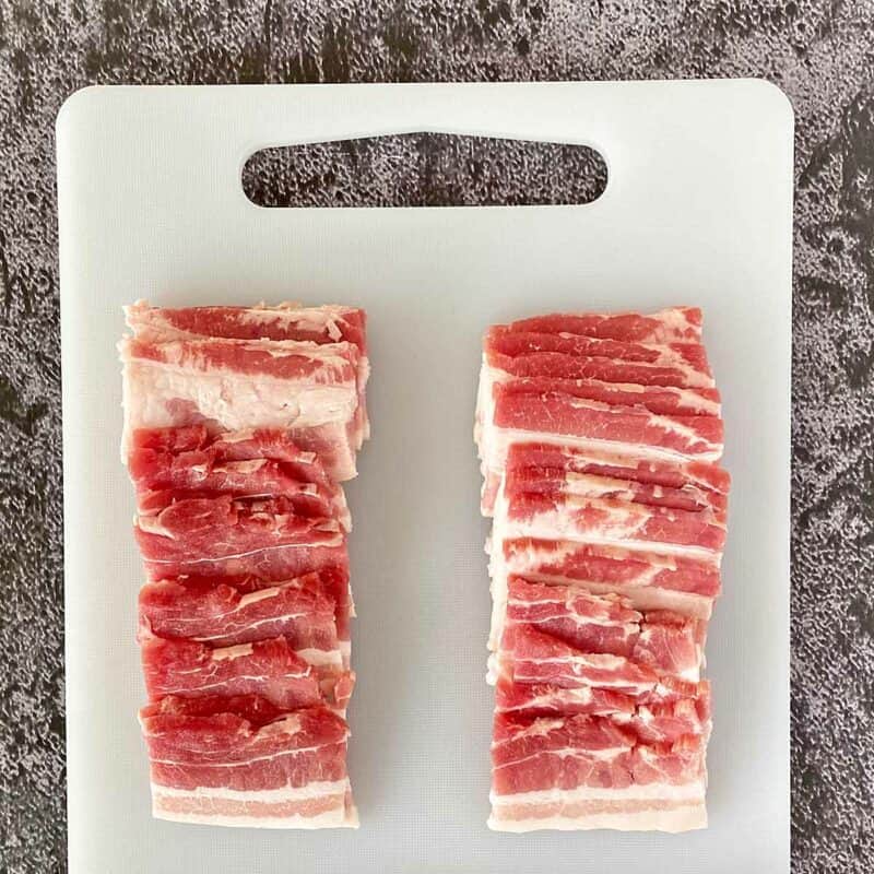 Two stacks of bacon pieces on a cutting board.