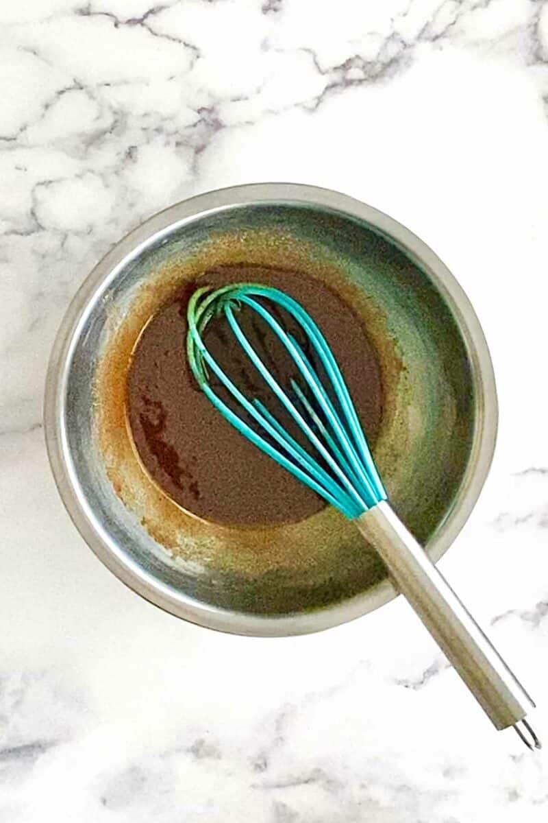 Mixing maple brown sugar glaze in a stainless steel bowl with a blue whisk.