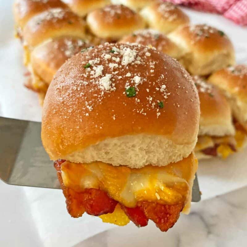 Dishing up a breakfast slider with melted cheddar and bacon using a metal spatula.