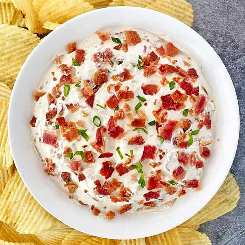 A white bowl filled with bacon horseradish dip surrounded by potato chips.