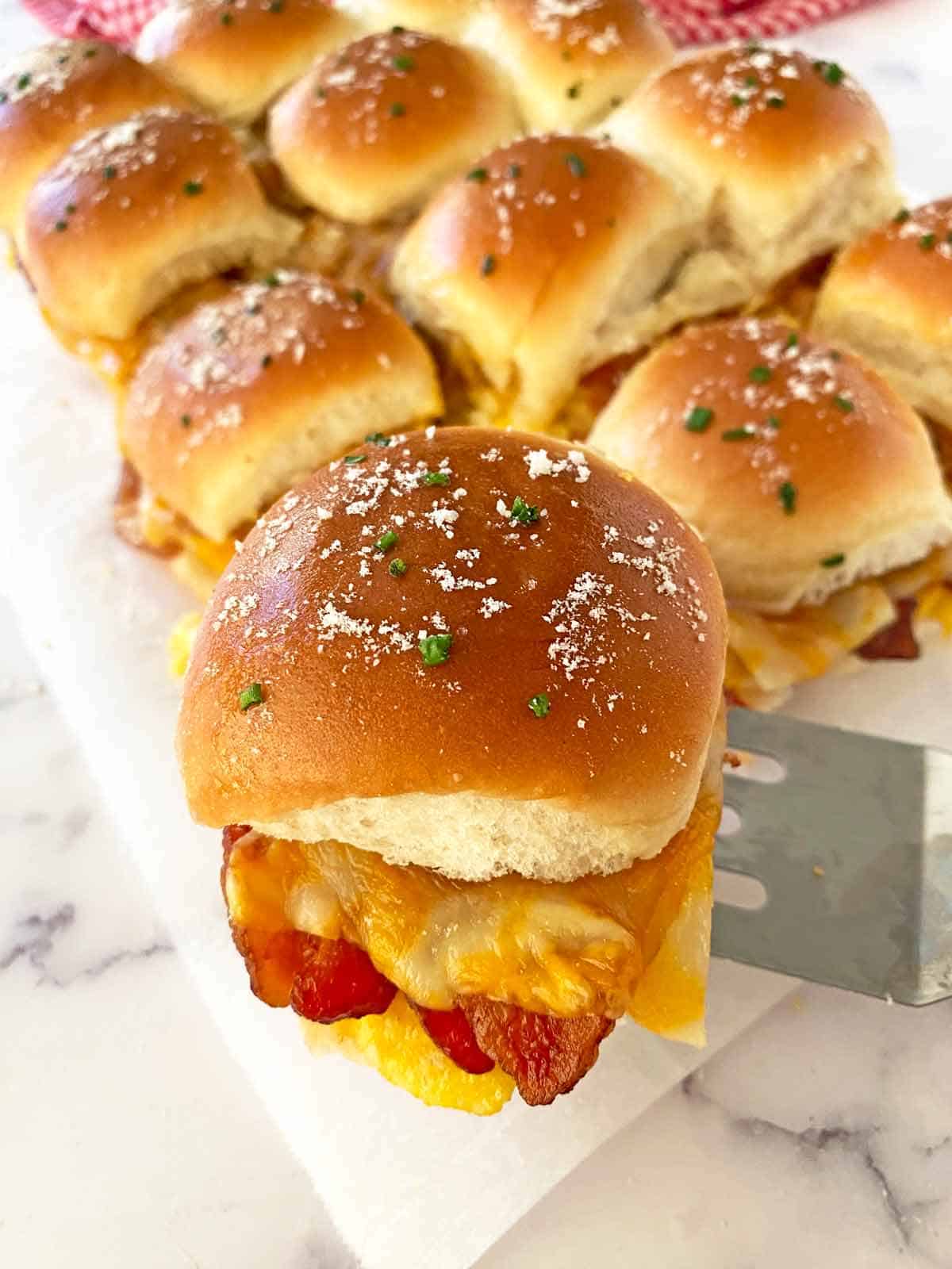 Serving a breakfast slider with bacon and cheese using a spatula.