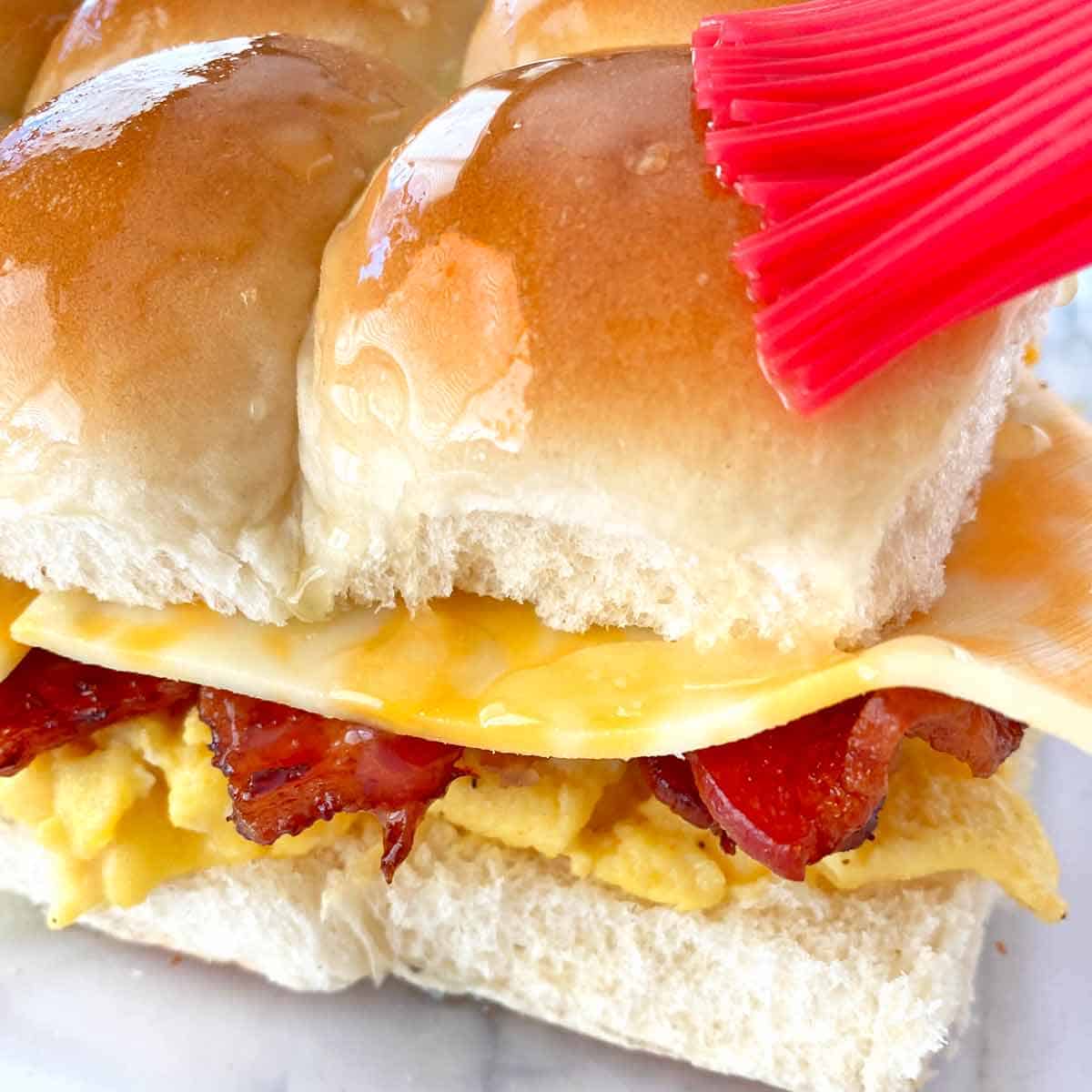 Brushing breakfast sliders with melted butter before baking.