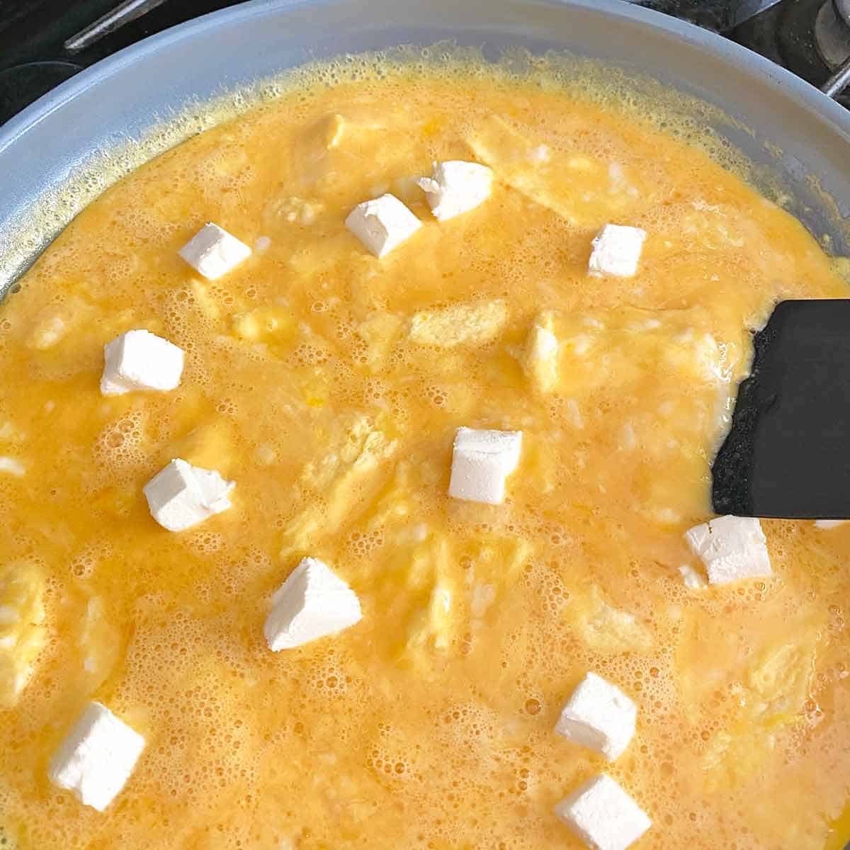 Adding cubes of cream cheese to the scrambled eggs.