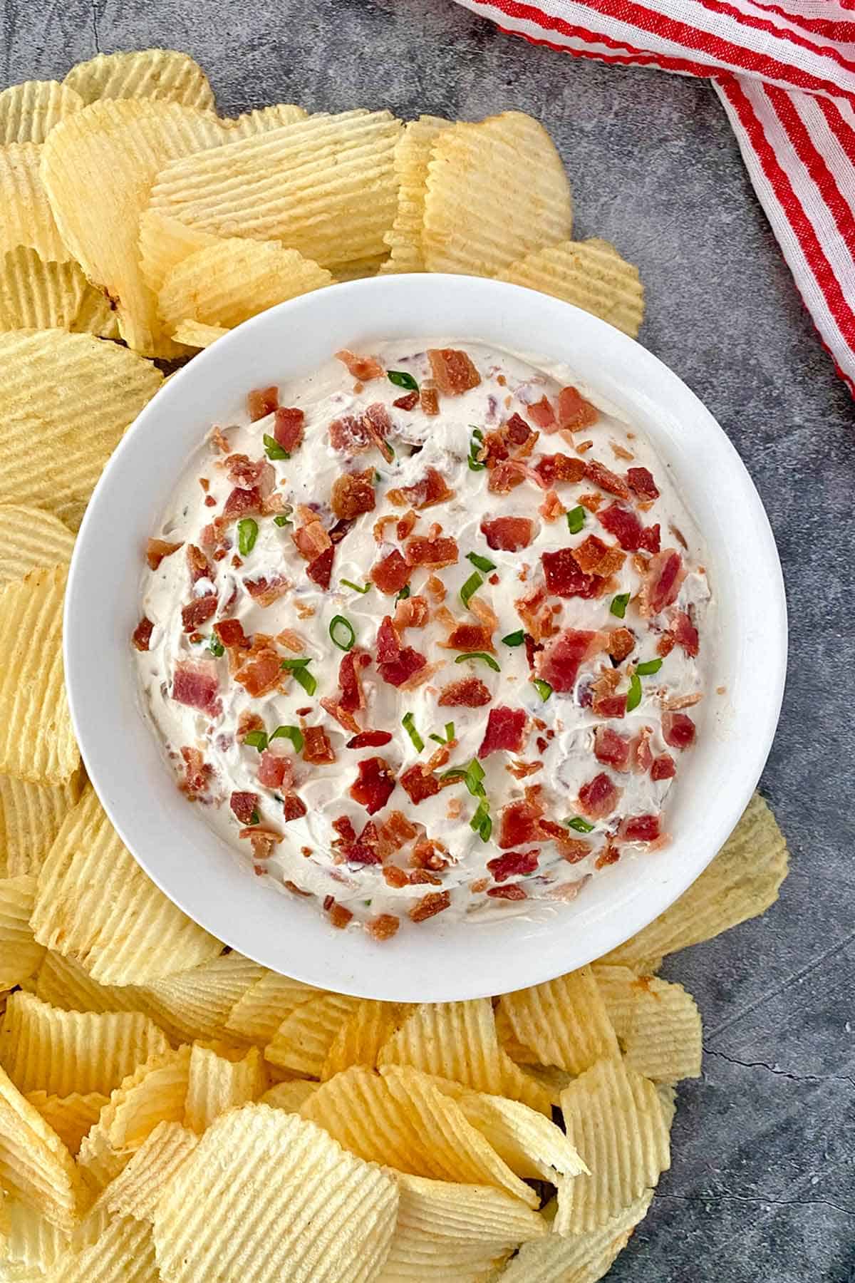 A bowl of horseradish dip with bacon surrounded by ridged potato chips.