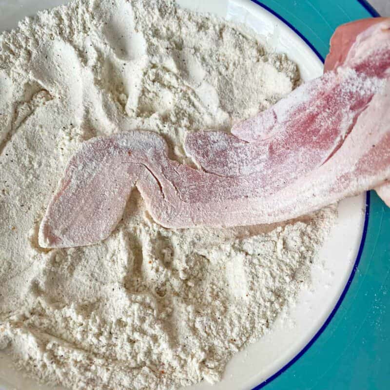 Lightly coating the uncooked bacon strip with the flour mixture.