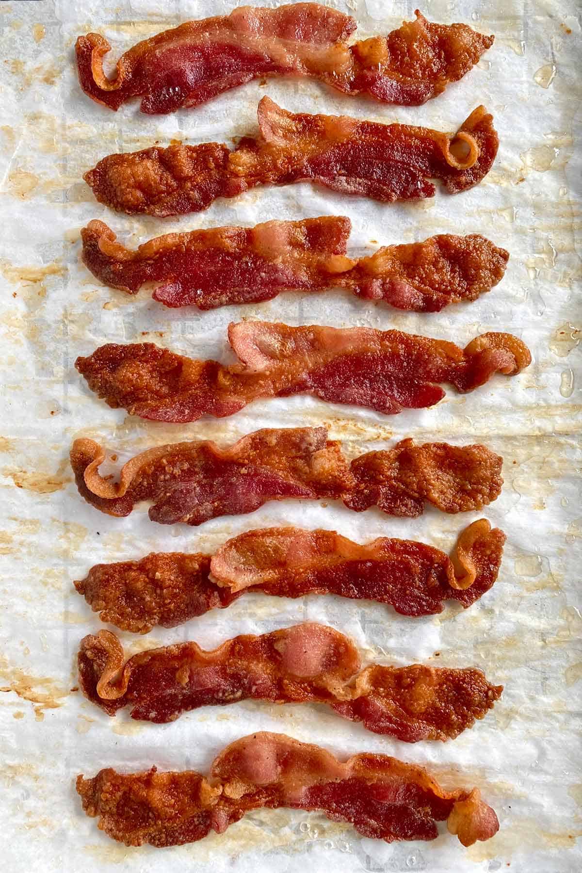 Eight strips of golden brown bacon cooked with flour on a baking sheet.