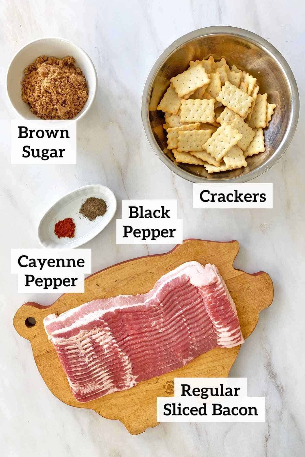 Crackers, brown sugar, seasonings and regular sliced bacon on a cutting board.