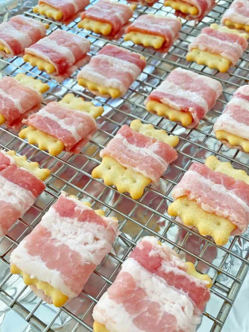 Two dozen bacon wrapped crackers on a wire rack on a sheet pan.