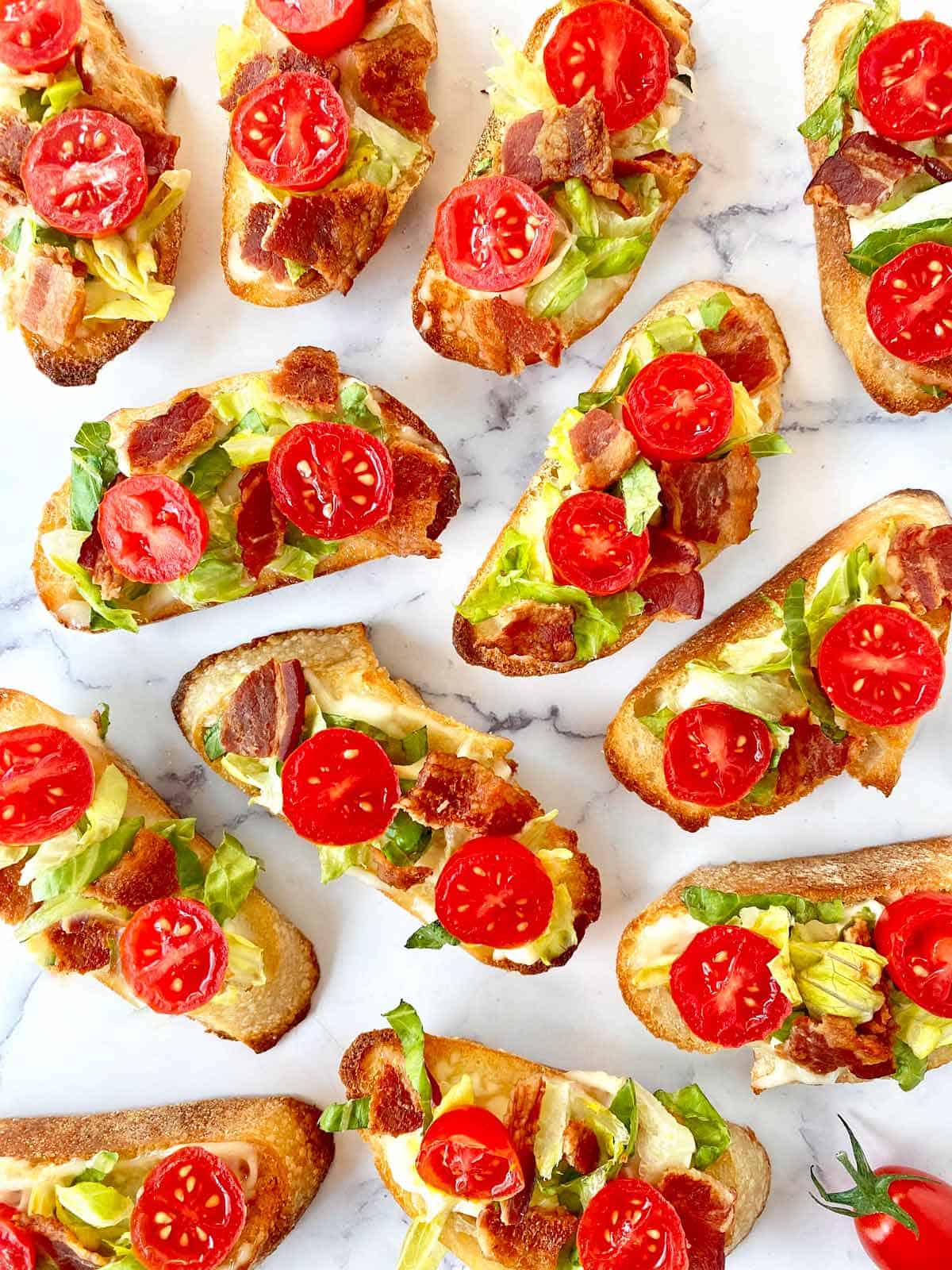 A dozen BLT crostini appetizers on a marble counter.