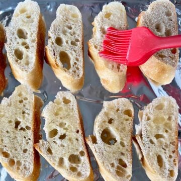 Brushing melted butter on baguette slices on a baking pan.