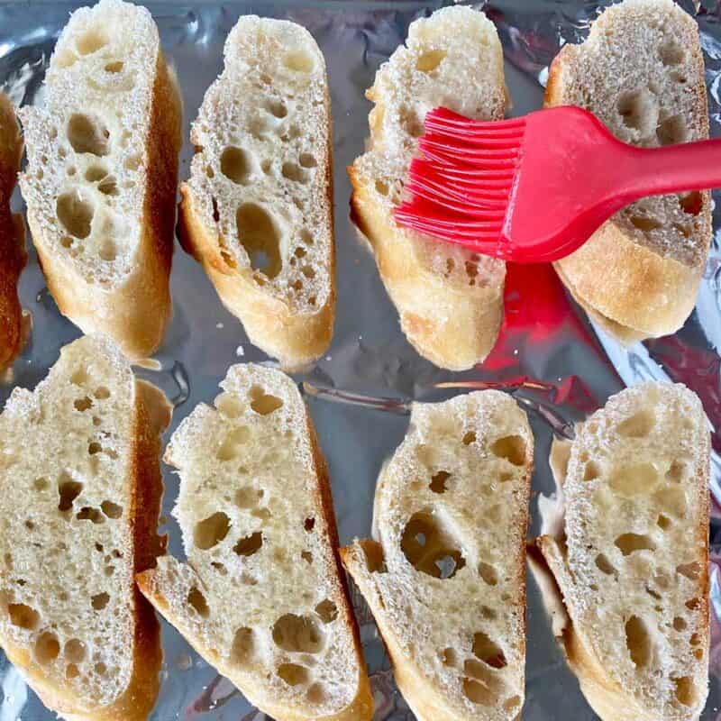 Brushing melted butter on baguette slices on a baking pan.