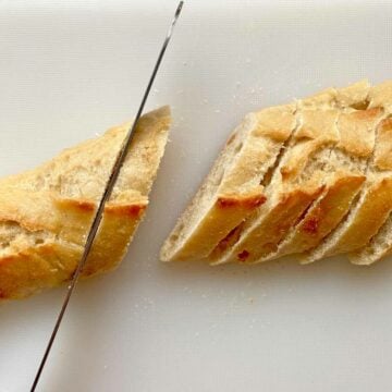 Using a serrated knife to cut a baguette in diagonal slices.